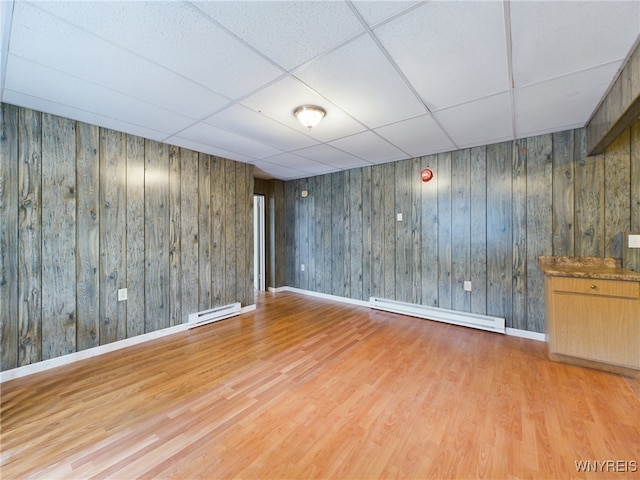 basement featuring a drop ceiling, a baseboard heating unit, and light hardwood / wood-style floors