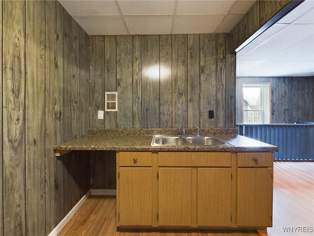 kitchen with a drop ceiling, wooden walls, sink, and light wood-type flooring