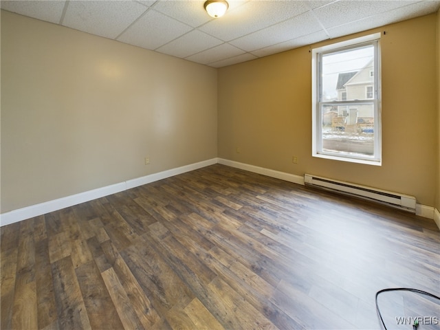 empty room featuring a baseboard heating unit, dark wood-type flooring, and a paneled ceiling