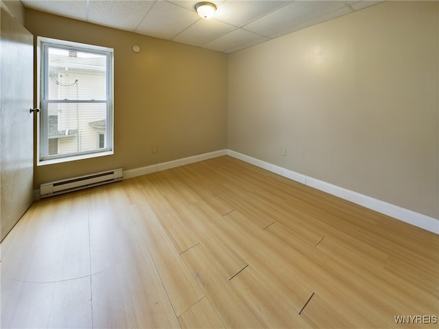 spare room with wood-type flooring, a baseboard heating unit, and a paneled ceiling