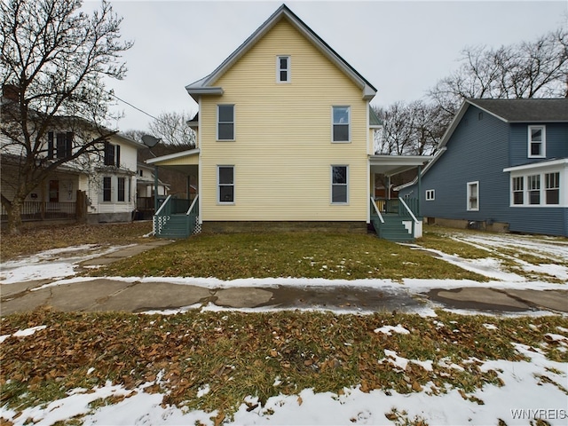 snow covered rear of property with a yard and covered porch