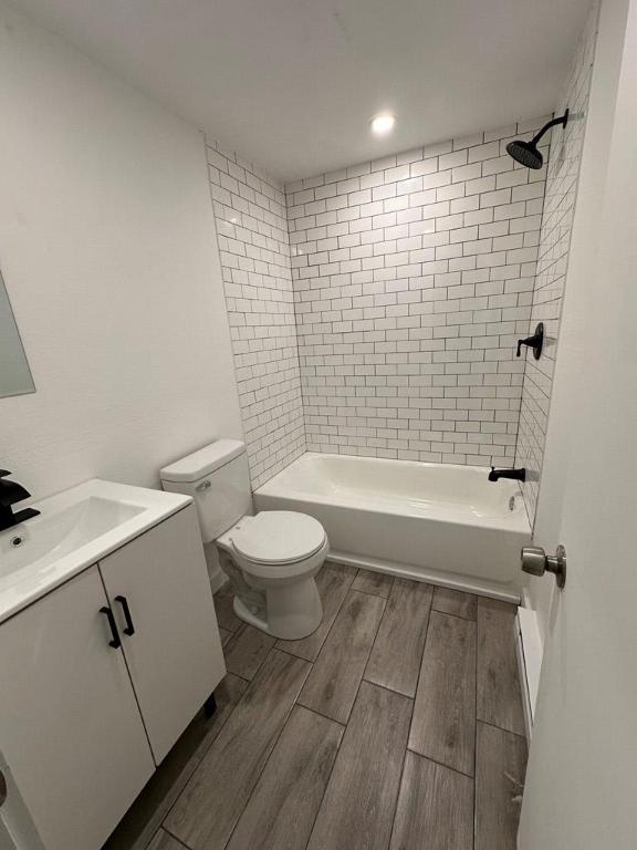 bathroom featuring toilet, wood tiled floor, shower / washtub combination, and vanity