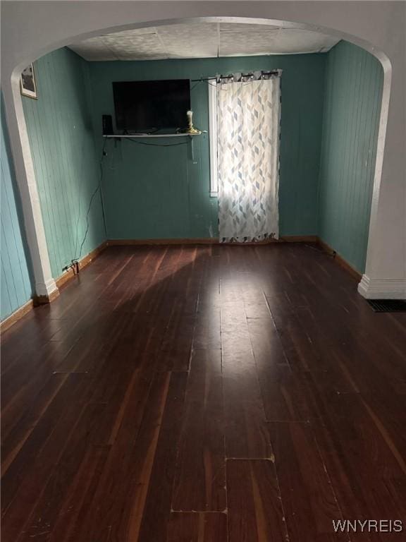 unfurnished room with arched walkways, wood-type flooring, and baseboards