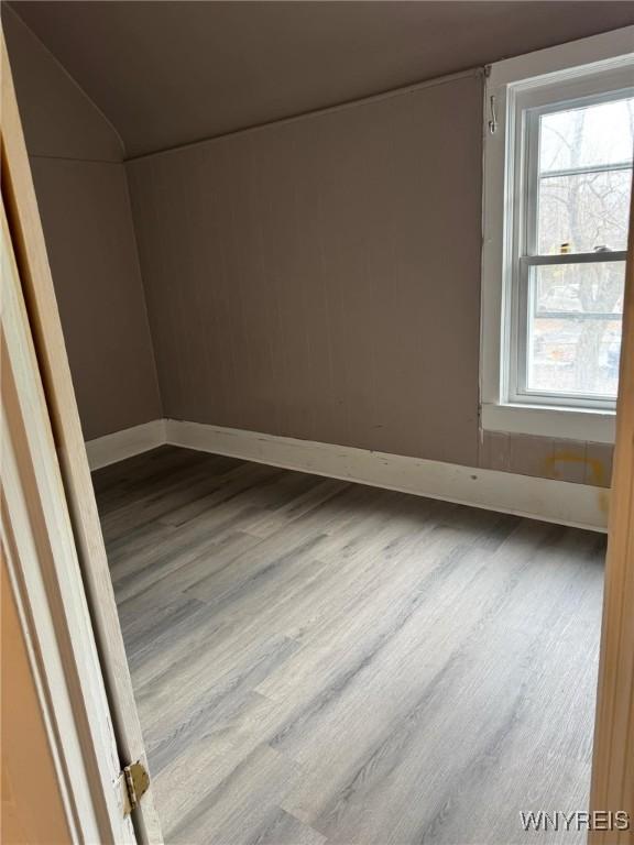 unfurnished room featuring lofted ceiling, baseboards, and wood finished floors