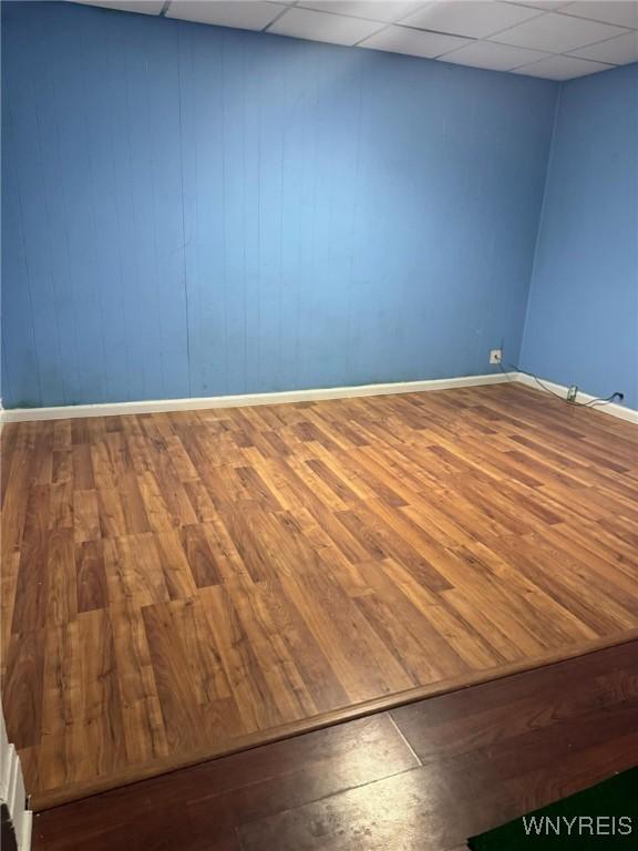 empty room with a paneled ceiling, baseboards, and wood finished floors