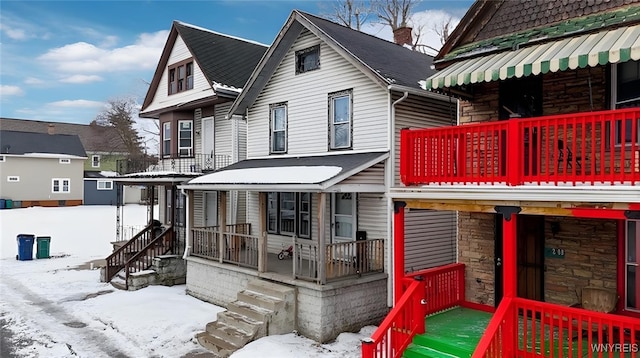 snow covered back of property featuring covered porch