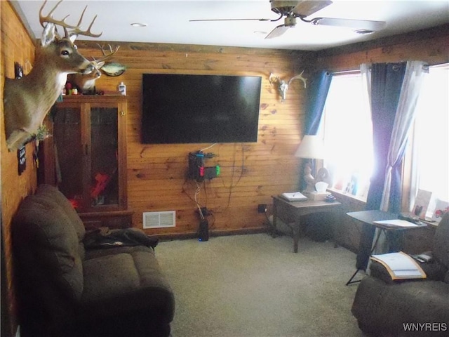 carpeted living room with ceiling fan and wood walls