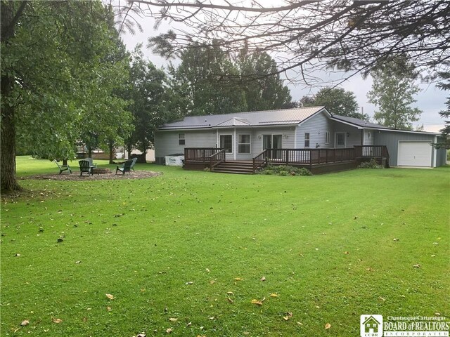 rear view of house featuring a garage, a lawn, a deck, and an outdoor fire pit