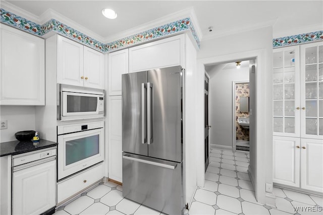 kitchen featuring crown molding, white appliances, dark stone countertops, and white cabinets