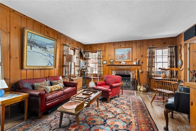 living room featuring wooden walls, wood-type flooring, a fireplace, and a textured ceiling