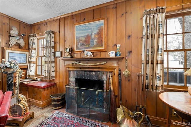 living room featuring a tiled fireplace, wood walls, a textured ceiling, and light hardwood / wood-style flooring