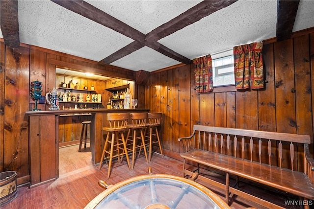 bar with hardwood / wood-style floors, a textured ceiling, beamed ceiling, and wood walls