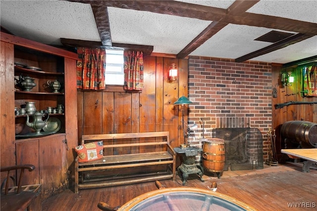 bar with hardwood / wood-style floors, wooden walls, a fireplace, a textured ceiling, and beamed ceiling