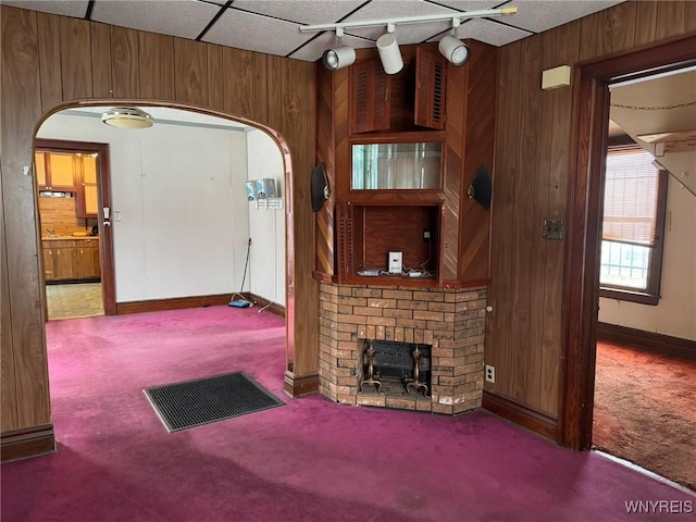 unfurnished living room featuring carpet, track lighting, a fireplace, and wood walls