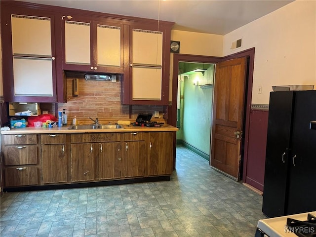 kitchen featuring tasteful backsplash, black fridge, sink, and hanging light fixtures