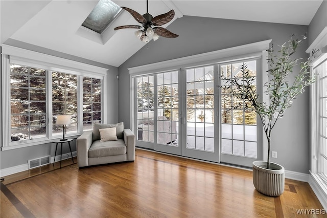 living area with wood-type flooring, vaulted ceiling with skylight, and ceiling fan