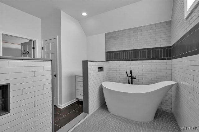 bathroom with lofted ceiling, a tub to relax in, tile patterned flooring, and tile walls