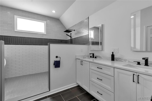 bathroom featuring tile patterned flooring, vanity, lofted ceiling, and a tile shower