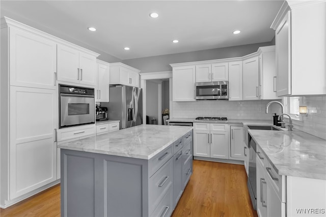 kitchen with white cabinetry, sink, a center island, stainless steel appliances, and light stone countertops