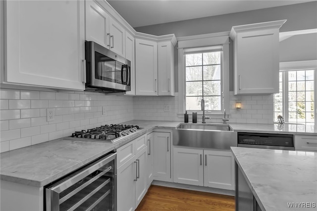 kitchen featuring sink, appliances with stainless steel finishes, beverage cooler, light stone countertops, and white cabinets