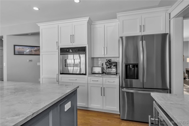 kitchen with appliances with stainless steel finishes, white cabinets, decorative backsplash, light hardwood / wood-style floors, and light stone counters