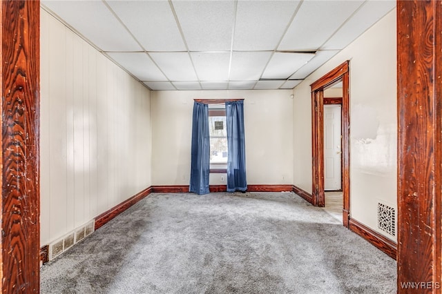 carpeted empty room with wooden walls and a drop ceiling