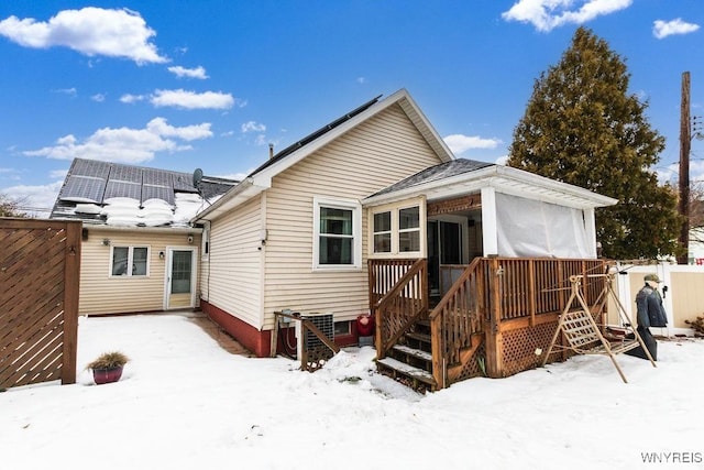 snow covered house with central AC unit, a sunroom, a deck, and solar panels