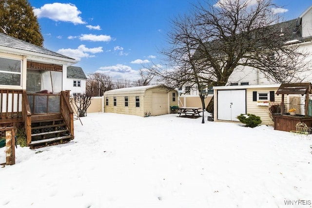 yard layered in snow with a wooden deck and a storage shed