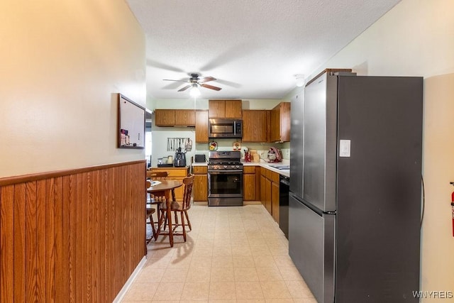 kitchen with ceiling fan, stainless steel appliances, a textured ceiling, and wood walls