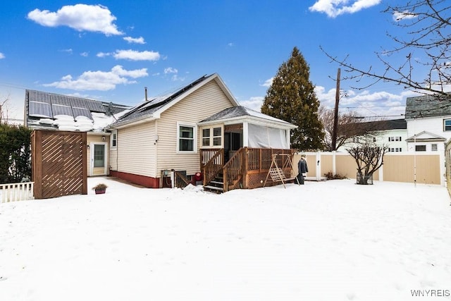 snow covered back of property with a wooden deck and solar panels