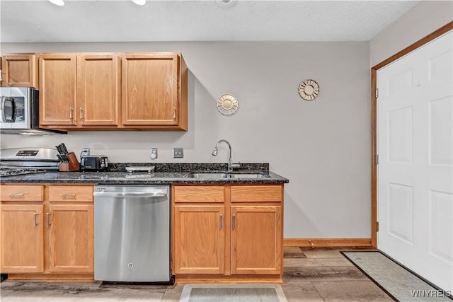 kitchen with stainless steel appliances, sink, light wood-type flooring, and dark stone counters