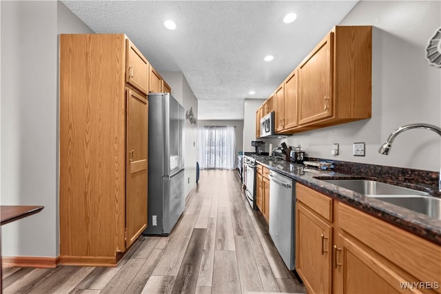 kitchen featuring sink, dark stone countertops, stainless steel appliances, a textured ceiling, and light hardwood / wood-style flooring