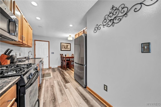 kitchen featuring appliances with stainless steel finishes, sink, a textured ceiling, and light wood-type flooring