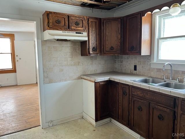 kitchen with a sink, light floors, backsplash, and under cabinet range hood