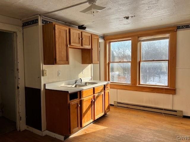 kitchen with a sink, brown cabinets, a baseboard radiator, and light wood finished floors