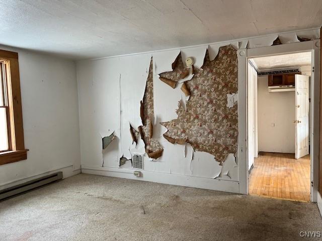 empty room featuring an AC wall unit, a baseboard heating unit, and carpet