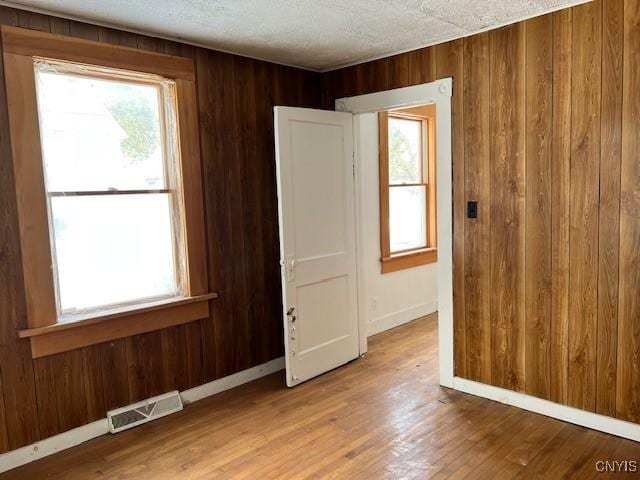 empty room featuring visible vents, plenty of natural light, and wooden walls