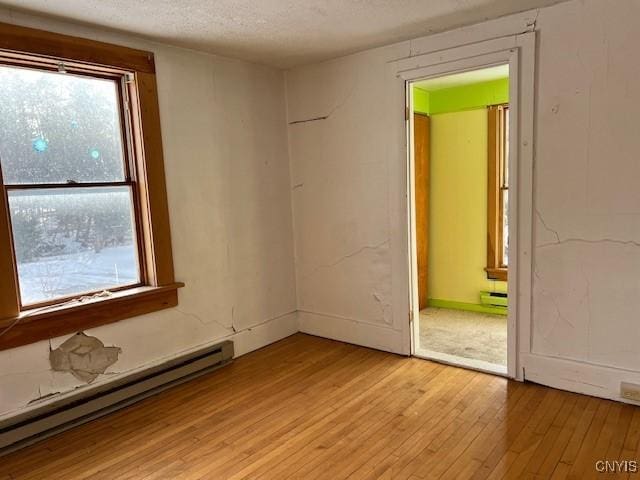 unfurnished room featuring a textured ceiling, a healthy amount of sunlight, light wood-style flooring, and a baseboard radiator