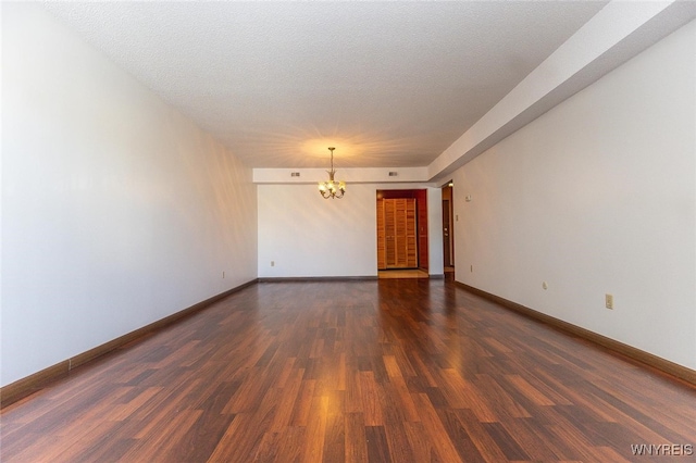 empty room featuring dark hardwood / wood-style flooring, a textured ceiling, and a chandelier