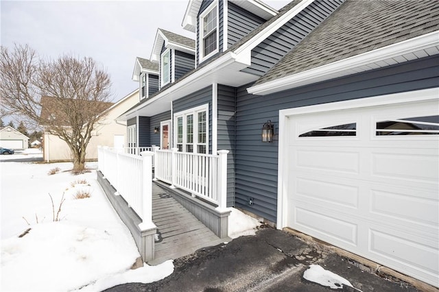 snow covered property entrance featuring a garage and covered porch