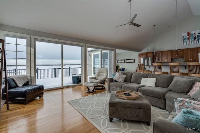 living room featuring ceiling fan, a water view, high vaulted ceiling, and light wood-type flooring