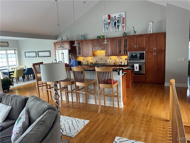 kitchen with hanging light fixtures, light hardwood / wood-style floors, a kitchen bar, and stainless steel appliances