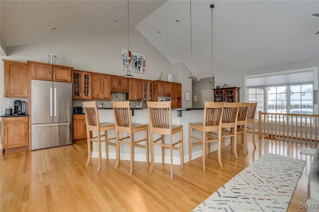 kitchen featuring a breakfast bar, decorative light fixtures, stainless steel fridge, light hardwood / wood-style floors, and backsplash