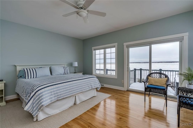 bedroom featuring multiple windows, a water view, access to exterior, and light hardwood / wood-style flooring