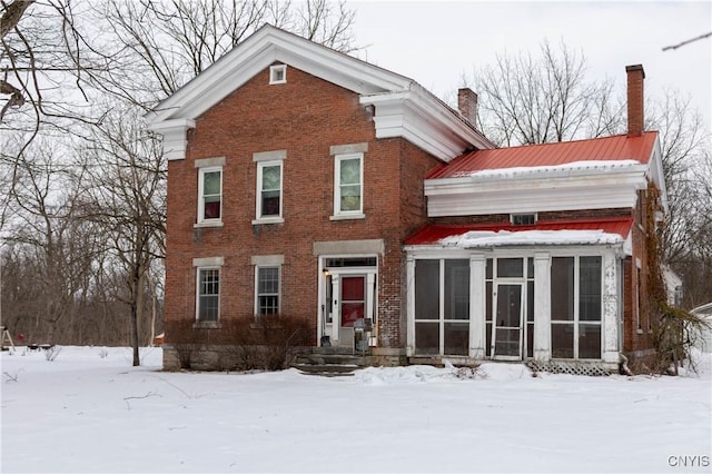 greek revival house with a sunroom, a chimney, and brick siding