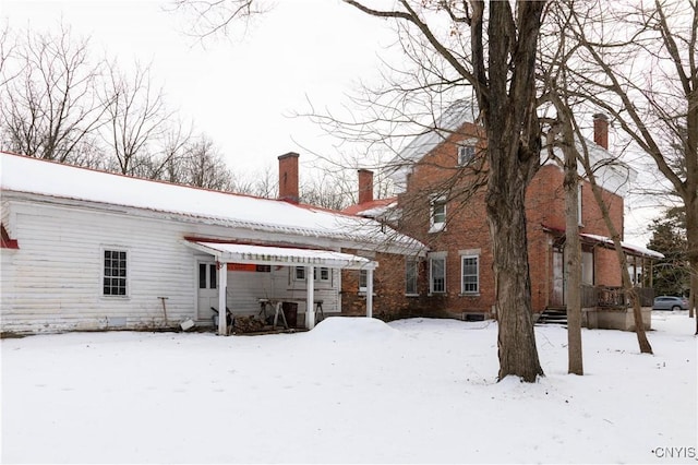 snow covered rear of property featuring a chimney