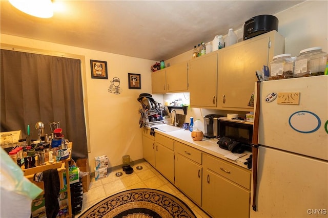 kitchen with light tile patterned floors, light countertops, freestanding refrigerator, a sink, and baseboards