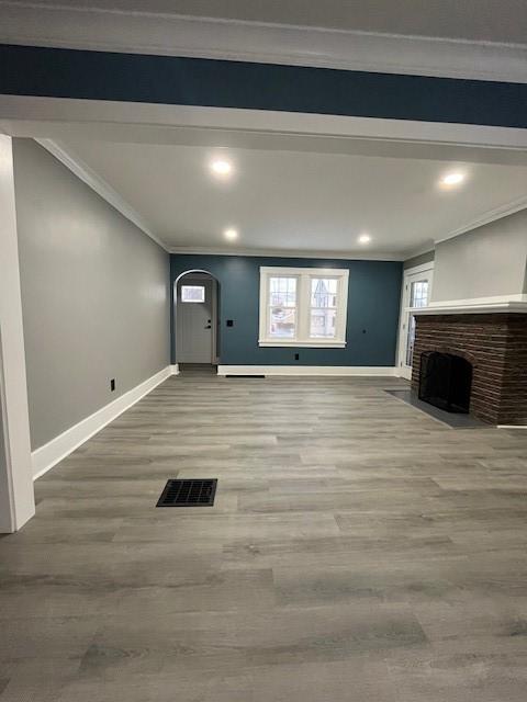 unfurnished living room featuring crown molding, a brick fireplace, and hardwood / wood-style flooring