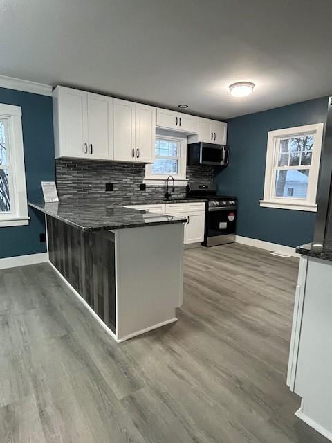 kitchen featuring backsplash, hardwood / wood-style floors, stainless steel appliances, white cabinets, and kitchen peninsula