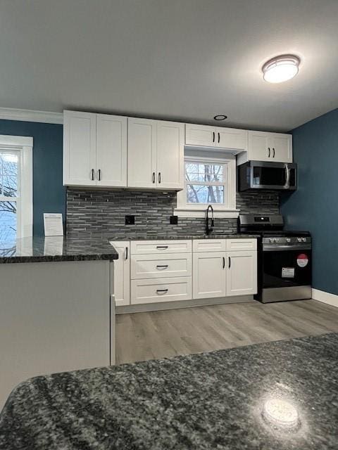 kitchen with white cabinetry, backsplash, dark stone counters, and appliances with stainless steel finishes